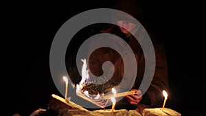 a man in a cloak with a hood is reading a hot book with candles on the floor