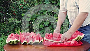 A man close-up cuts a slice of watermelon into equal parts with a knife.