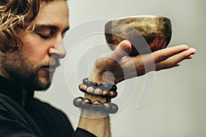 A man with closed eyes listens to the singing bowls. A man holds singing bowls in front of him. The rosary on hand.