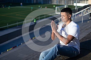 Man with closed eyes sitting on stadium bleachers while praying