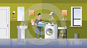 Man with clothes basket standing near washing machine guy doing housework laundry room modern bathroom interior male