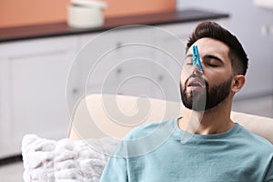 Man with clothespin suffering from runny nose at home. Space for text