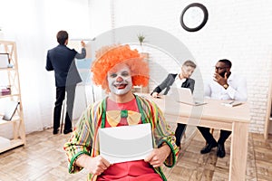 A man in a clown suit and a wig is sitting in the business office on April 1.