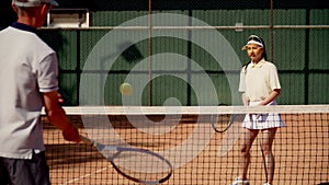 A man coach with a ward girl conduct a joint training tennis set at light intensity. The serving and deflecting blows