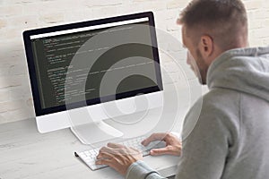 Man coding app on a computer. Close-up scene. Clean office desk with brick wall in background