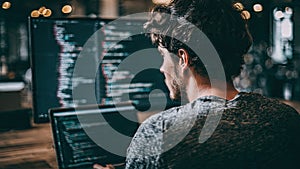 Man coding on computer with multiple screens in a dimly lit environment