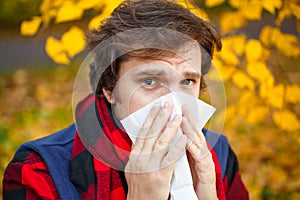 Man with cold rhinitis on autumn background. Fall flu season. Il