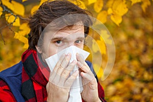 Man with cold rhinitis on autumn background. Fall flu season. Il