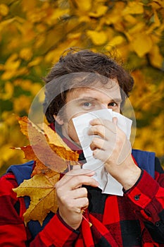 Man with cold rhinitis on autumn background. Fall flu season. Il