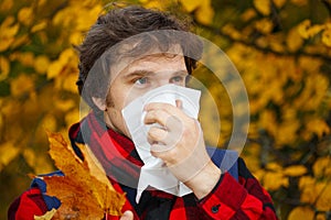 Man with cold rhinitis on autumn background. Fall flu season. Il