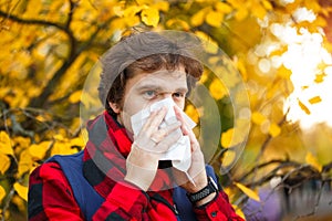 Man with cold rhinitis on autumn background. Fall flu season. Il