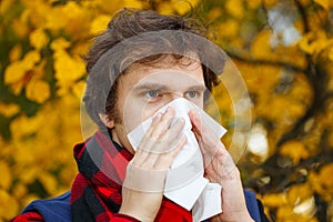 Man with cold rhinitis on autumn background. Fall flu season. Il