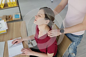 Man colleague massages shoulders of tired woman with hands