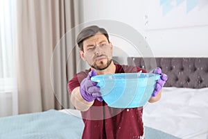 Man collecting leaking water from ceiling in bedroom.