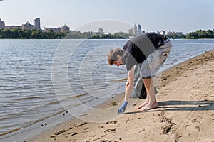 Man collecting plastic waste from a polluted beach using a garbage collector. Environmental problems, environmental pollution.