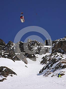 Man in colorful outfit skiiing down a very steep snow couloir under a cable car station in the Swiss Alps in deep winter