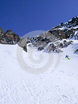 Man in colorful outfit skiiing down a very steep snow couloir under a cable car station in the Swiss Alps in deep winter