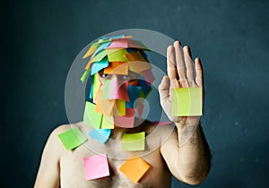 Man with colorful sticky notes all over his face and body show palm hand making stop gesture