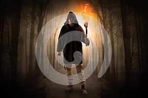 Man coming from dark forest with burning flambeau in his hand concept