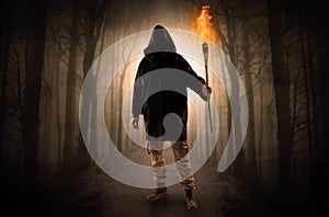 Man coming from dark forest with burning flambeau in his hand concept