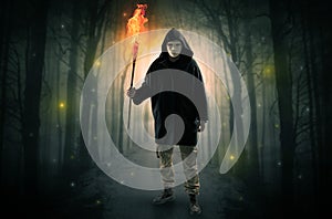 Man coming from dark forest with burning flambeau in his hand concept