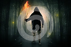 Man coming from dark forest with burning flambeau in his hand concept