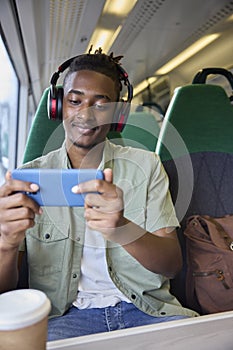 Man Commuting To Work Sitting On Train Streaming And Watching Film Or Show On Mobile Phone