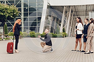 A man in the company of friends meets his girlfriend with luggage at the airport makes an offer to a red-haired girl