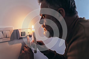 Man in complete darkness holding a candle to investigate thermostat during a power outage. Blackout concept