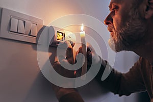 Man in complete darkness holding a candle to investigate thermostat during a power outage. Blackout concept