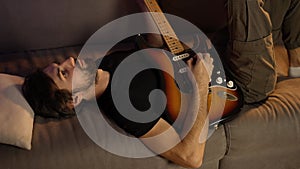Man composing music on guitar while lying on couch
