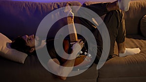 Man composing music on guitar while lying on sofa