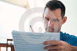 Man Composing Music Using Score Sheets To Write Notes Down