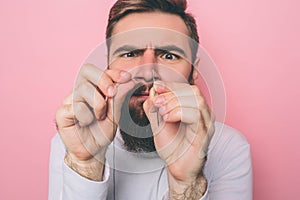 Man is concentrated. He is putting the thread in the eye of a needle. Isolated on pink background.