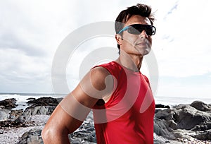 Man, confidence and beach for fitness, health and wellness in activewear, sunglasses and cloudy sky. Male, jog and