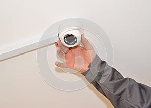 The man configures the surveillance camera on a room ceiling photo