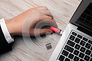 Man connecting usb flash drive to laptop at white wooden table, top view