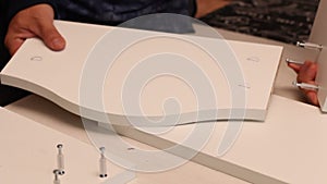 A man connects elements of a table shelf. He pulls them together with eccentrics. Self-assembly of furniture. Close-up