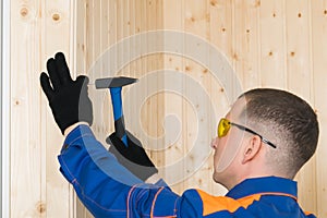 Man in construction clothes and goggles nails the board with nails and a hammer