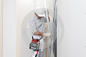 Man construction worker or plasterer holding drywall metal profiles near plasterboard white wall in building site. Wearing white