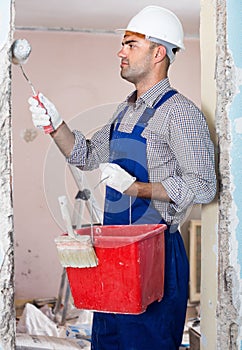 Man constructor in helmet plastering wall with roller