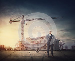 Man contractor or architect wearing protective helmet stands confident on the rooftop in front of a construction site with working