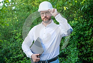 Man contractor in hardhat holding laptop outdoors