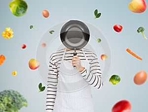 Man or cook in apron hiding face behind frying pan