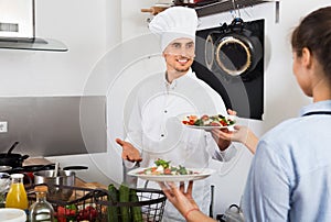 Man cook giving to waitress ready to serve salad