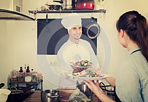 Man cook giving to waitress ready to serve salad