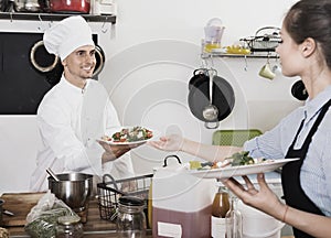Man cook giving to waitress ready to serve salad