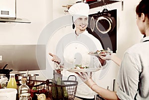 Man cook giving to waitress ready to serve salad