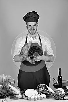 Man in cook hat and apron with salad. Cook works in kitchen with vegetables and tools.
