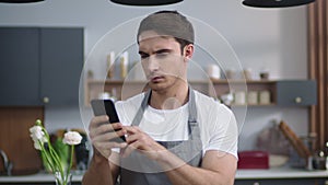 Man cook searching recipe on mobile phone. Chef looking phone screen at kitchen.